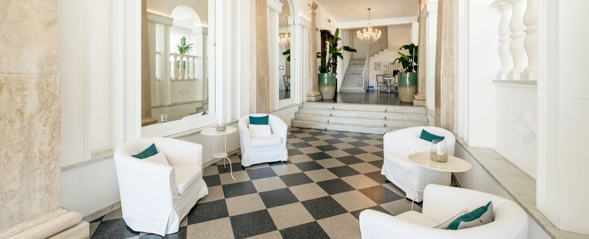 Elegante hall con poltrone bianche, pavimento a scacchi e scale con piante.