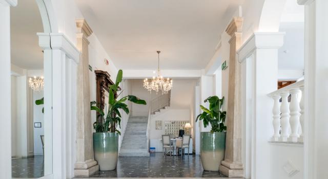 Elegante ingresso con piante, lampadari e scale in marmo bianco.